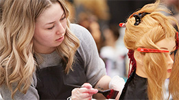 A hairstyling student applying dye to a mannequin