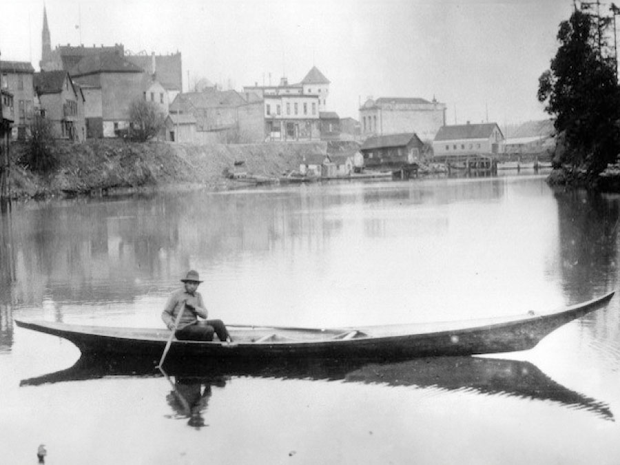an old photo of a man steering a canoe
