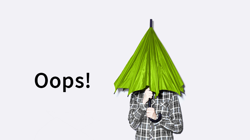A person hiding below half-closed green umbrella, with the word oops written next to it
