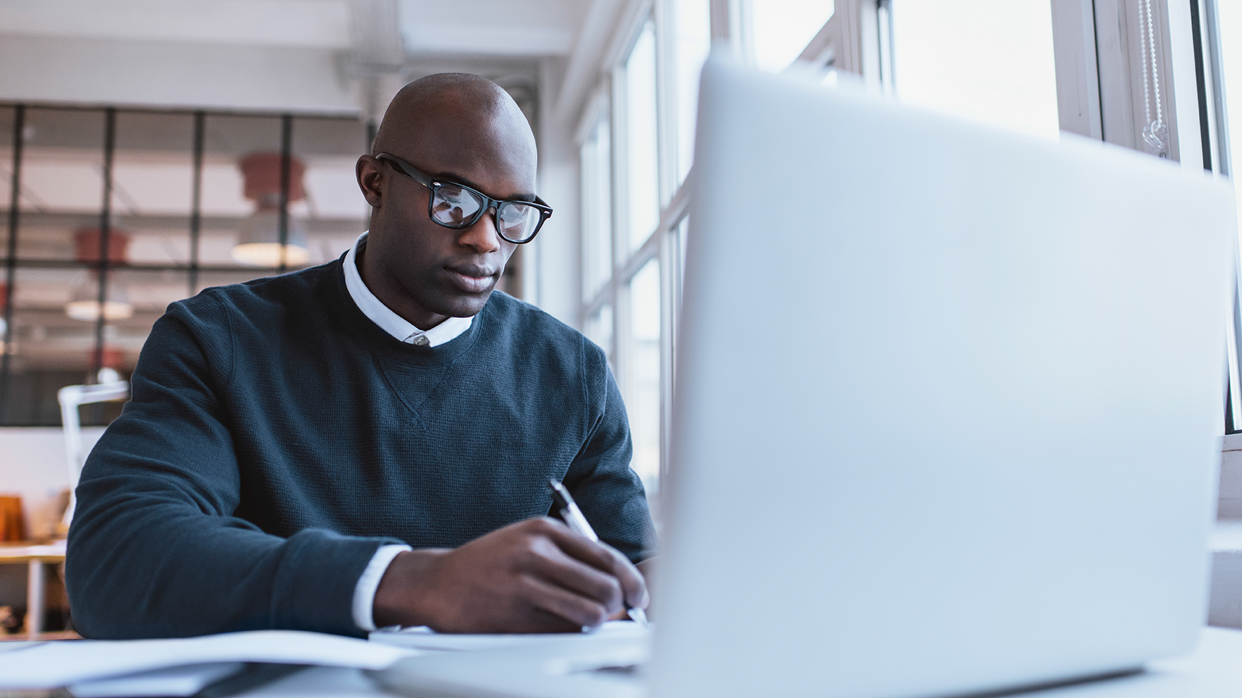 A man with dark glasses, working next to a laptop